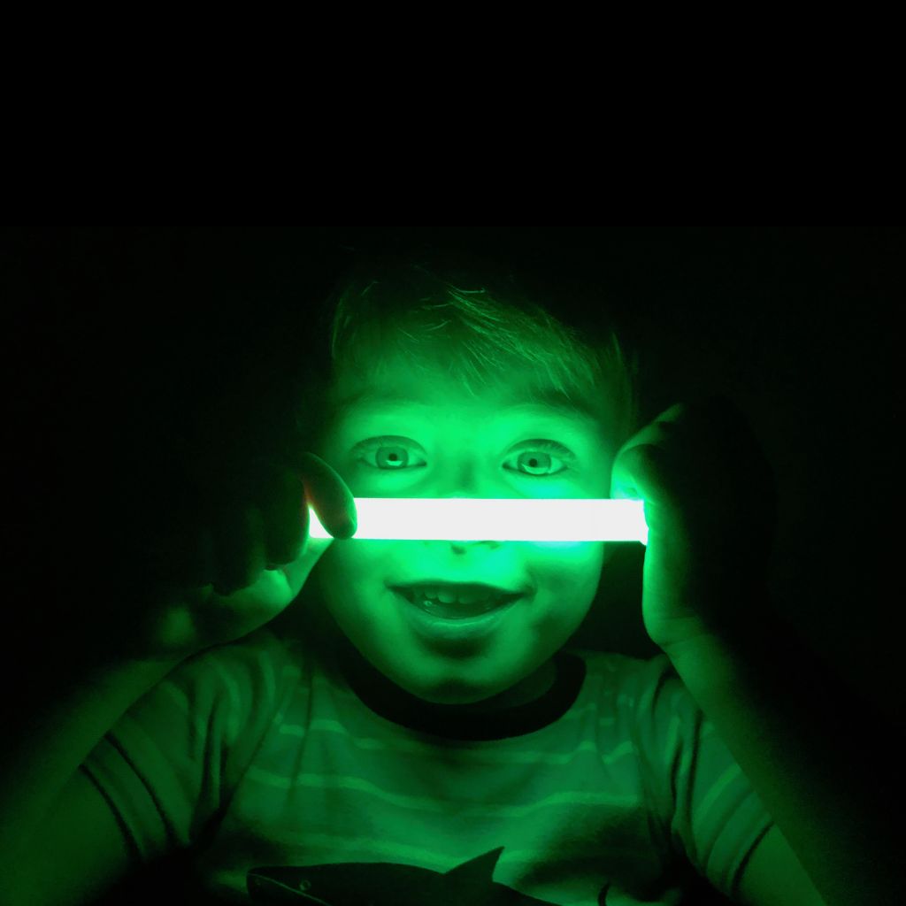 a young boy holding a green light up in the dark